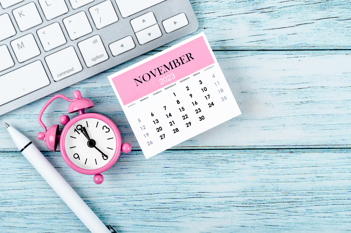 The November 2023 Monthly calendar year and alarm clock with keyboard computer on wooden background.