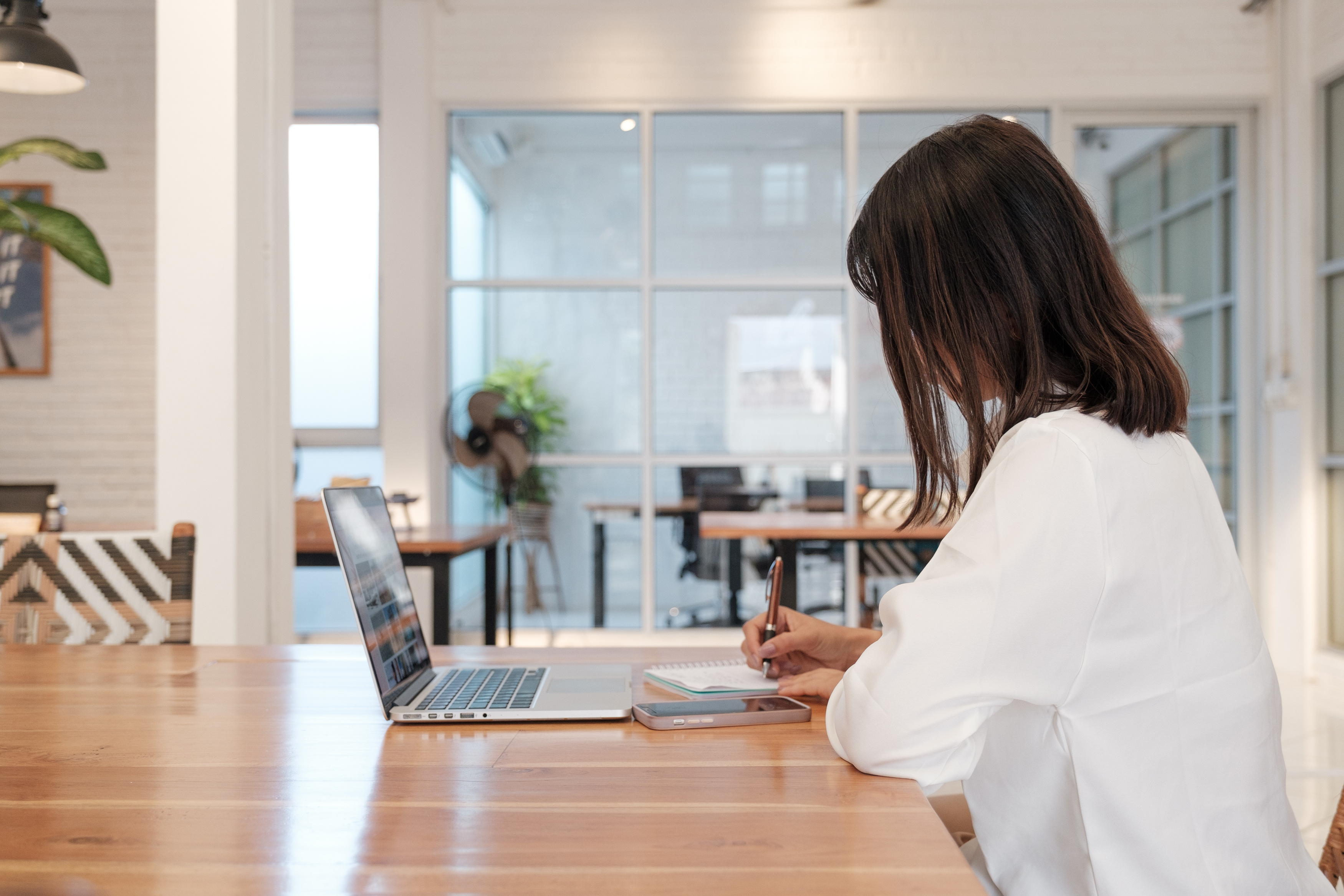 Woman Writing Notes with Smartphone and Laptop on Workspace